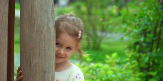 小女孩的肖像在孩子们的操场上隐藏和恐惧，微笑和大笑。快乐的孩子在绿色的夏日公园玩耍。