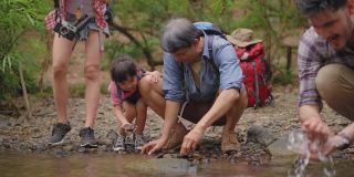 一个亚洲大家庭带着一个孩子，坐在小溪边休息，爸爸，爷爷，妈妈洗着汗，女儿和爷爷奶奶玩得很开心，心情激动，在热带森林探险和徒步旅行。