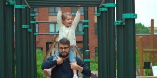 爸爸和小女儿在院子里的户外操场上做运动。幸福的家庭，小女孩和爸爸玩活跃的游戏