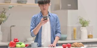 年轻的亚洲男子站在厨房里用智能手机聊天