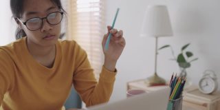亚洲女孩正紧张地坐在家里，在笔记本电脑上与导师在线学习。提出在家在线学习的概念
