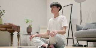 年轻的亚洲男子在瑜伽垫上做伸展运动在家