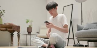 年轻的亚洲男子在瑜伽垫上使用智能手机