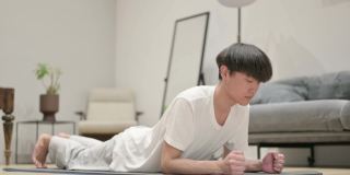 年轻的亚洲男子在瑜伽垫上做平板支撑
