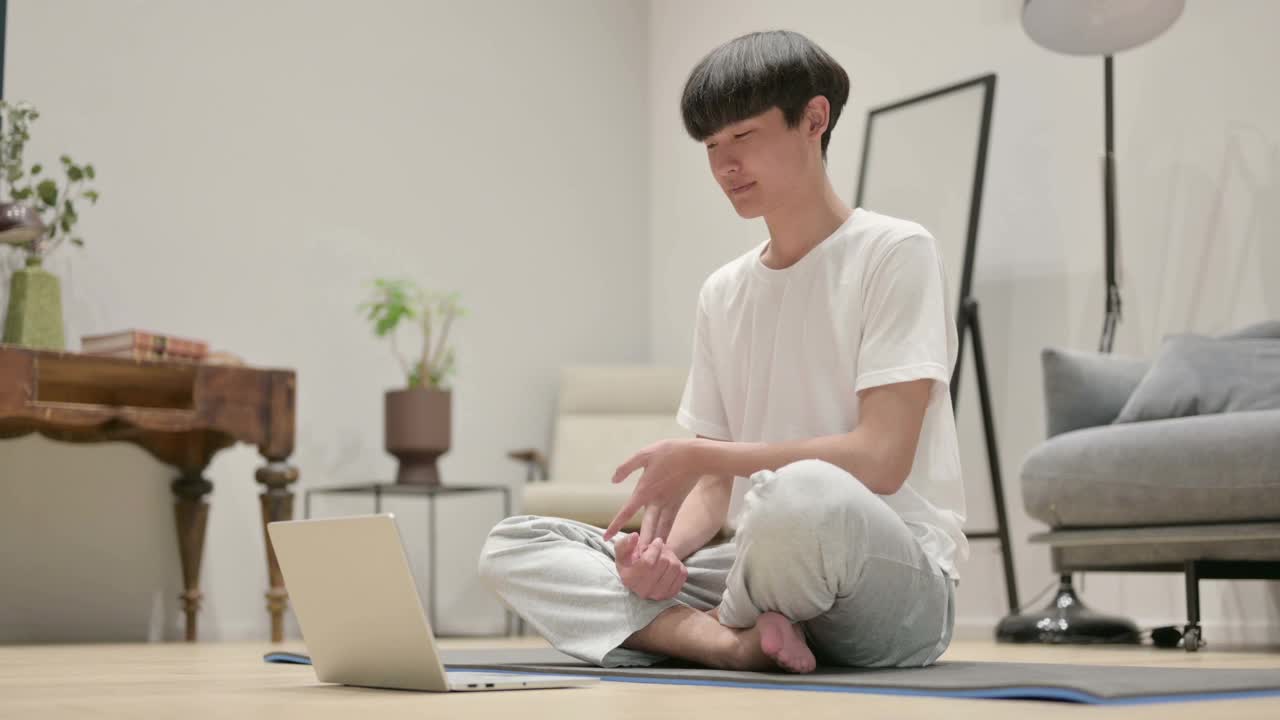 年轻的亚洲男子在瑜伽垫上使用笔记本电脑