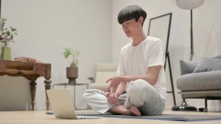 年轻的亚洲男子在瑜伽垫上使用笔记本电脑视频素材模板下载