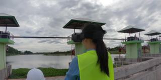 女工程师戴着白色头盔和黄色制服，戴着vr -头戴式虚拟现实眼镜，想象未来在建筑工地修建大坝发电。