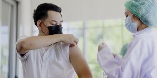 COVID-19疫苗接种站。医生或护士正在病房为男性患者接种COVID-19或流感疫苗。人们在诊所或医院办公室佩戴口罩以预防病毒感染