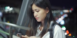 在泰国，一名年轻女子晚上站在走廊上使用智能手机。
