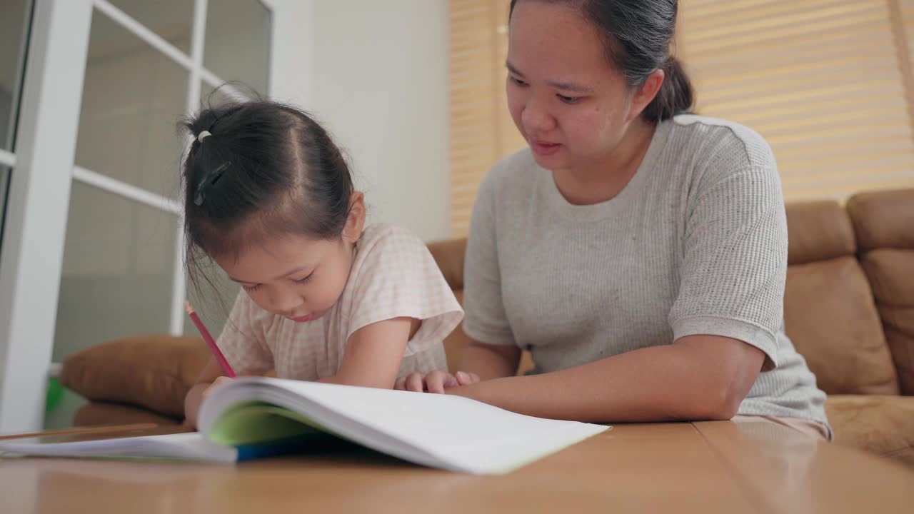 亚洲母亲照顾她的小女孩学习写在学校作业在家里