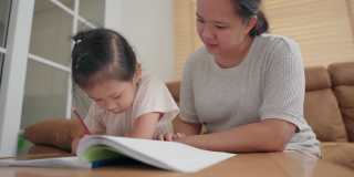 亚洲母亲照顾她的小女孩学习写在学校作业在家里