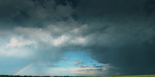 戏剧性的天空与雨云和彩虹雨后在地平线上乡村景观乡村道路通过田野。农业和天气预报概念。时间流逝，时间流逝，时间流逝全高清视图蓝色多云戏剧性的天空时间流逝