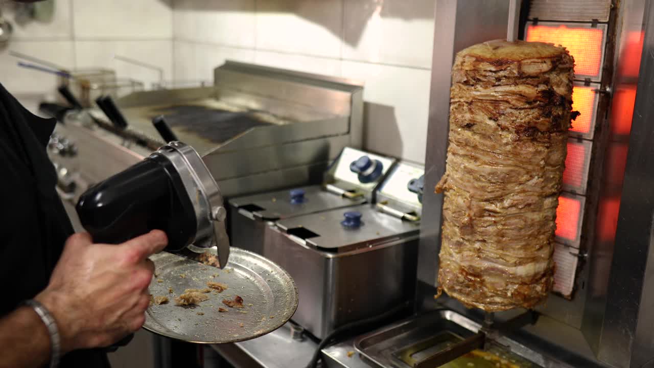 在希腊餐厅的厨房里，厨师用电动工具把鸡陀螺从陀螺烤架上切下来