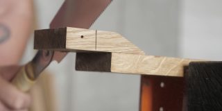 木匠用手锯锯一块橡木板。用手锯从橡木板上锯一块木头的木匠。手工木工工具在工作。木工的艺术。手工木工工具的声音
