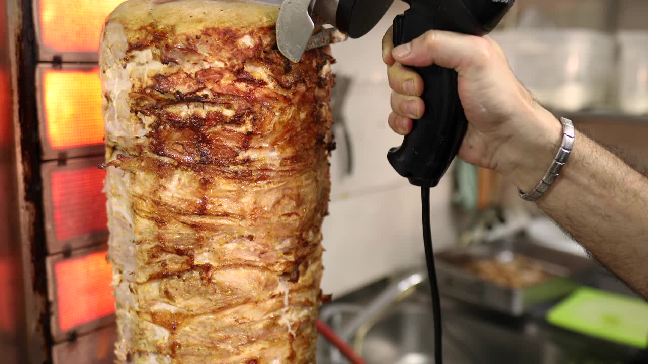 在他的希腊餐厅里，厨师用电动旋转刀从陀螺烤架上切陀螺