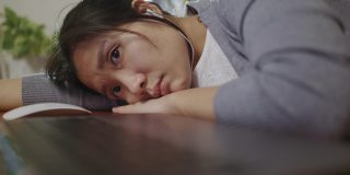 一个亚洲女人把下巴放在桌子上，表现出了极大的厌倦。努力工作。