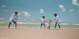 亚洲爸爸和妈妈在夏天的海滩上和孩子玩拔河游戏。父母和孩子们去海边度假。幸福的家庭关系和团队合作理念。慢动作镜头
