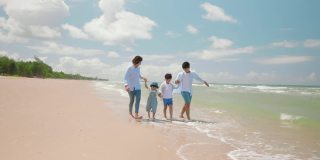 亚洲的爸爸和妈妈在夏天和孩子一起玩，沿着海滩散步。父母和孩子们去海边度假。幸福家庭关系理念。慢动作