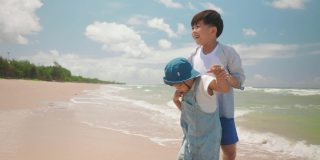 慢镜头快乐的两个亚洲男孩孩子在夏天的一天在海滩玩水。家庭中的兄弟姐妹关系