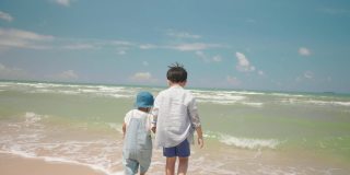 慢镜头快乐的两个亚洲男孩孩子在夏天的一天在海滩玩水。家庭中的兄弟姐妹关系