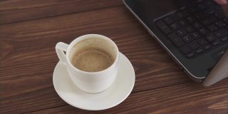 一个女人在家里用电脑工作，喝咖啡。一台笔记本电脑，一杯加酱的白咖啡