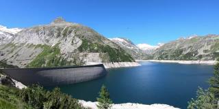 全景式的人工湖在科隆布雷因大坝在卡林西亚，奥地利。大坝被高山积雪覆盖的山峰包围着。陡峭的斜坡。这个湖是深蓝色的。自然能源