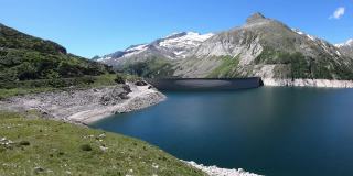 全景式的人工湖在科隆布雷因大坝在卡林西亚，奥地利。大坝被高山积雪覆盖的山峰包围着。陡峭的斜坡。这个湖是深蓝色的。自然能源