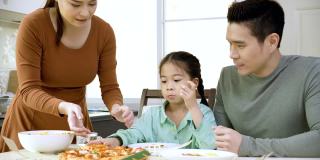 幸福的亚洲家庭，父母和可爱的小女儿早上在家里的厨房吃披萨。周末活动快乐家庭生活理念。呆在家里。庆祝你家庭的大日子。