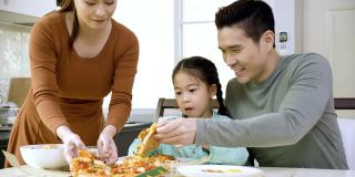 幸福的亚洲家庭，父母和可爱的小女儿早上在家里的厨房吃披萨。周末活动快乐家庭生活理念。呆在家里。庆祝你家庭的大日子。