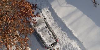 一个成年人在一场暴风雪后清理他的车。鸟瞰无人机正上方的慢动作视频。