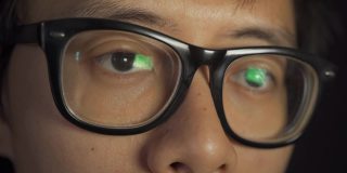 特写亚洲人的眼睛和脸与眼镜在电脑屏幕前工作在深夜。人们的生活方式。