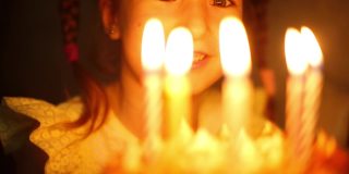 女孩看着蛋糕上燃烧的蜡烛，许了一个愿。生日，蜡烛的火焰，橘色的火焰，一个孩子幸福的眼睛。孩子们的节日。特写镜头
