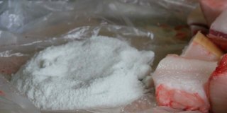 一名男性屠夫用盐将大块猪肉裹在肥肉和猪肉皮中