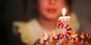 女孩看着蛋糕上写着数字5的燃烧的蜡烛，许了一个愿。生日，五周年，五年，烛火，橙火。孩子们的节日。特写镜头
