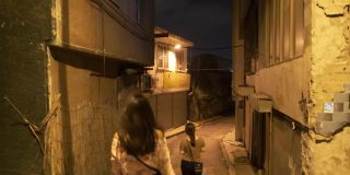 两个单独的年轻女性朋友漫步在小巷和小巷在午夜的黄色灯泡下旅游旅游参观好奇的地方观光步行概念4K分辨率