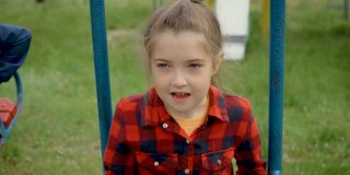 画一个小女孩穿着红衬衫在秋千上。年轻快乐的孩子用灰色的眼睛看着孩子们玩耍。好奇的孩子靠近