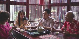 中国父亲与儿子在多代同堂期间享受传统的中秋节月饼和中国茶在家里下午茶聚会