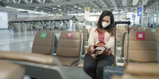 正面:只有亚洲女性穿着粉色t恤，戴着防护COVID-19的口罩，带着行李、护照、机票，在机场等待新的旅程、旅行、度假时使用智能手机、触摸社交媒体。