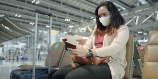 侧面低视角:只有亚洲女性穿着粉色t恤，戴着防护COVID-19的口罩，带着行李、护照、机票，在机场等待新的旅程、旅行、度假时使用智能手机、触摸社交媒体。