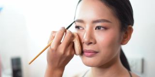 年轻的亚洲女孩在工作室的化妆过程的特写。专业化妆师制作明亮的化妆照片会话。