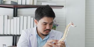 慢动作场景物理治疗师医生男人学习和阅读人体脊柱杂志在笔记本电脑上搜索信息和诊断背痛症状在医务室的健康和技术概念