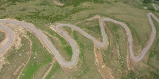 从山顶俯瞰穿过群山的山路。无人机拍摄到一条蜿蜒的道路穿过绿色的山丘和山脉。