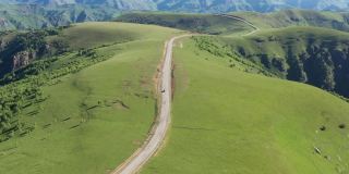 从山顶俯瞰穿过群山的山路。无人机拍摄到一条蜿蜒的道路穿过绿色的山丘和山脉。