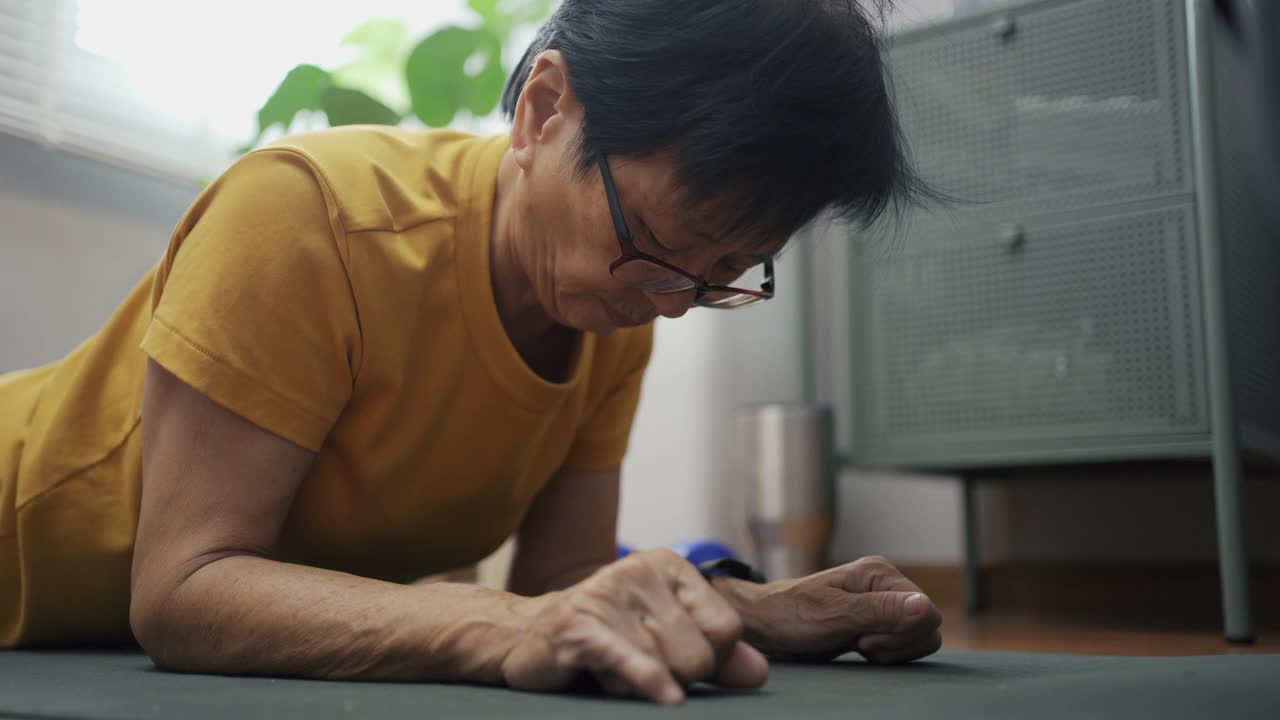 亚洲老年妇女在Covid - 19隔离期间跟随在线教程和在家锻炼。