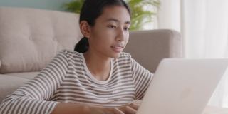 穿着长袖的亚洲女孩正在家里的客厅里使用笔记本电脑