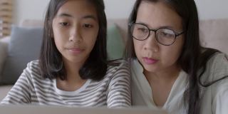 亚洲家庭与女儿做作业使用平板电脑与母亲的帮助