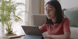 一个亚洲女孩通过一个带耳机的平板电脑与导师在线学习