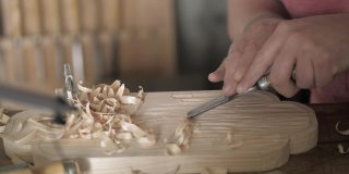 特写镜头。木雕师用凿子加工松木板。工匠在做一个茶盘。木工的艺术用手工木工工具工作。木工的声音