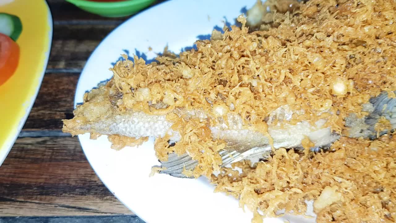 美味的印尼海鲜炒黑鲷鱼与油炸调味面糊，香料，浅盘与其他背景菜在印尼餐厅