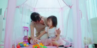 亚洲美丽慈爱的母亲花时间与年轻的小女孩女儿在客厅在家里。家长和孩子在帐篷里玩教育游戏，学习和发展技能。内部活动关系。
